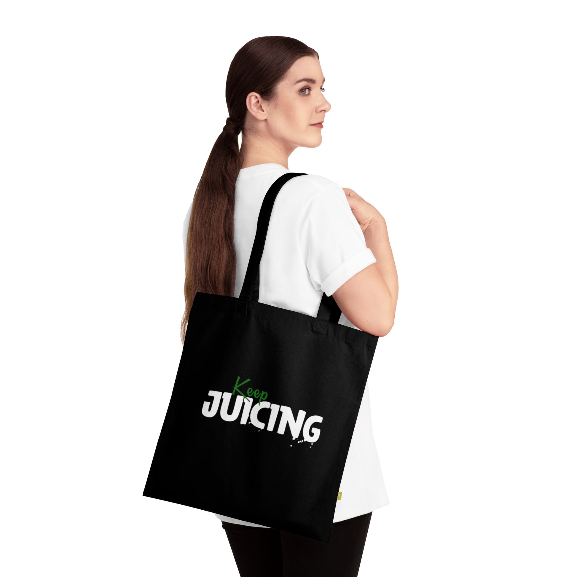 Woman carrying a black tote bag with 'Keep Juicing' text on a white background